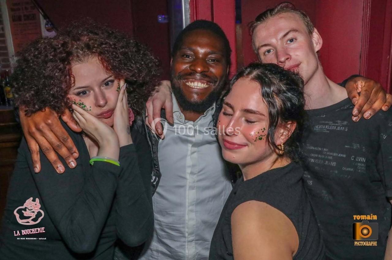 Quatre personnes souriantes posent ensemble dans un environnement festif, avec des décorations lumineuses sur leurs visages.