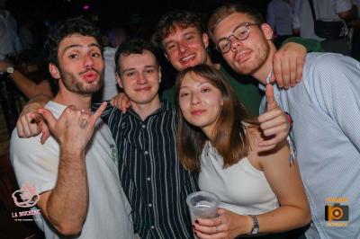 Un homme souriant avec des lunettes de soleil pose avec une femme dans un environnement festif et animé.