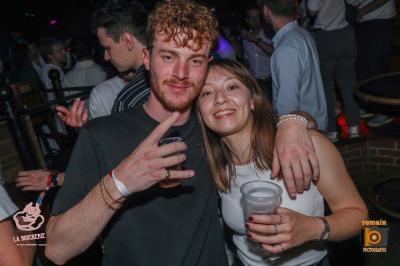 Un homme souriant avec des lunettes de soleil pose avec une femme dans un environnement festif et animé.