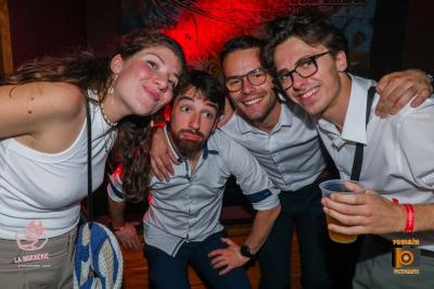 Un homme souriant avec des lunettes de soleil pose avec une femme dans un environnement festif et animé.