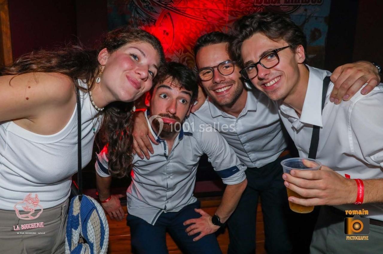 Quatre personnes souriantes posent ensemble dans un environnement festif, avec des lumières rouges en arrière-plan.