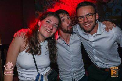 Un homme souriant avec des lunettes de soleil pose avec une femme dans un environnement festif et animé.