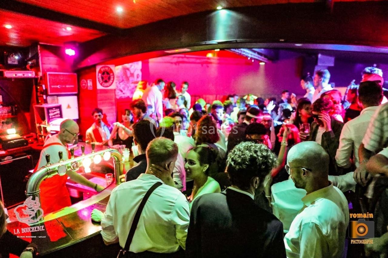 Un bar animé avec des clients discutant et un barman servant des boissons dans une ambiance lumineuse et festive.