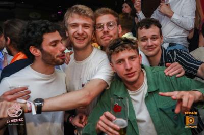 Un homme souriant avec des lunettes de soleil pose avec une femme dans un environnement festif et animé.