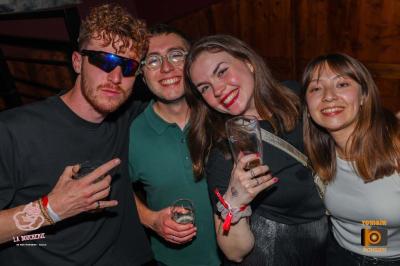 Un homme souriant avec des lunettes de soleil pose avec une femme dans un environnement festif et animé.