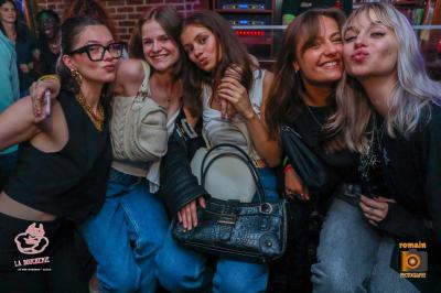 Un homme souriant avec des lunettes de soleil pose avec une femme dans un environnement festif et animé.
