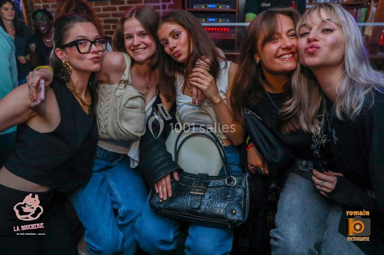 Cinq jeunes femmes souriantes posent ensemble dans un environnement festif avec un mur de briques en arrière-plan.
