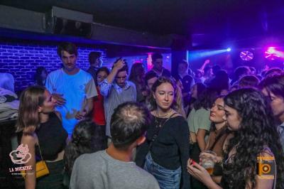 Un homme souriant avec des lunettes de soleil pose avec une femme dans un environnement festif et animé.