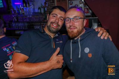 Un homme souriant avec des lunettes de soleil pose avec une femme dans un environnement festif et animé.