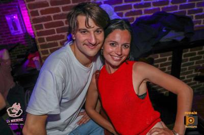 Un homme souriant avec des lunettes de soleil pose avec une femme dans un environnement festif et animé.