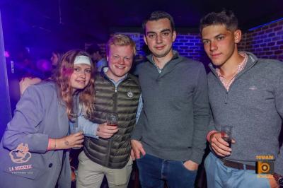 Un homme souriant avec des lunettes de soleil pose avec une femme dans un environnement festif et animé.