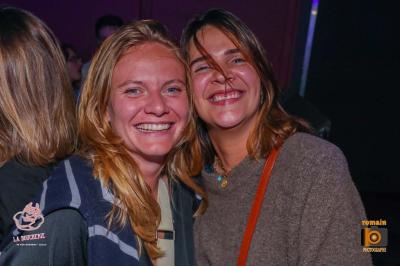 Un homme souriant avec des lunettes de soleil pose avec une femme dans un environnement festif et animé.