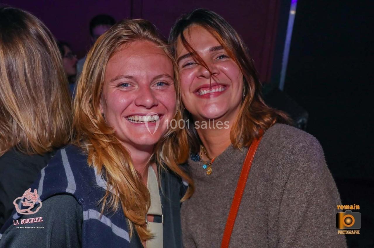 Deux femmes souriantes posent côte à côte dans un environnement intérieur sombre.