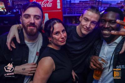 Un homme souriant avec des lunettes de soleil pose avec une femme dans un environnement festif et animé.