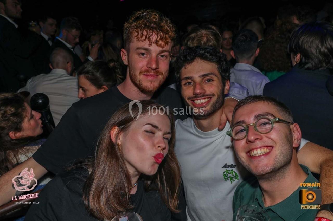 Quatre jeunes adultes souriants posent ensemble dans une ambiance festive et animée.