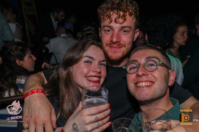 Un homme souriant avec des lunettes de soleil pose avec une femme dans un environnement festif et animé.