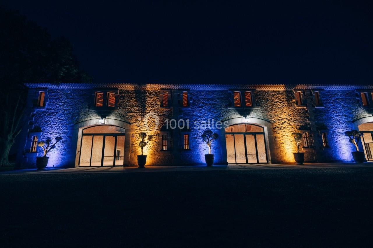 Façade d'un bâtiment en pierre éclairée par des lumières bleues et orange dans un environnement nocturne.
