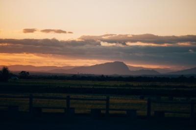 Paysage au coucher du soleil avec des champs, une clôture en bois et des montagnes à l'horizon sous un ciel partiellement…