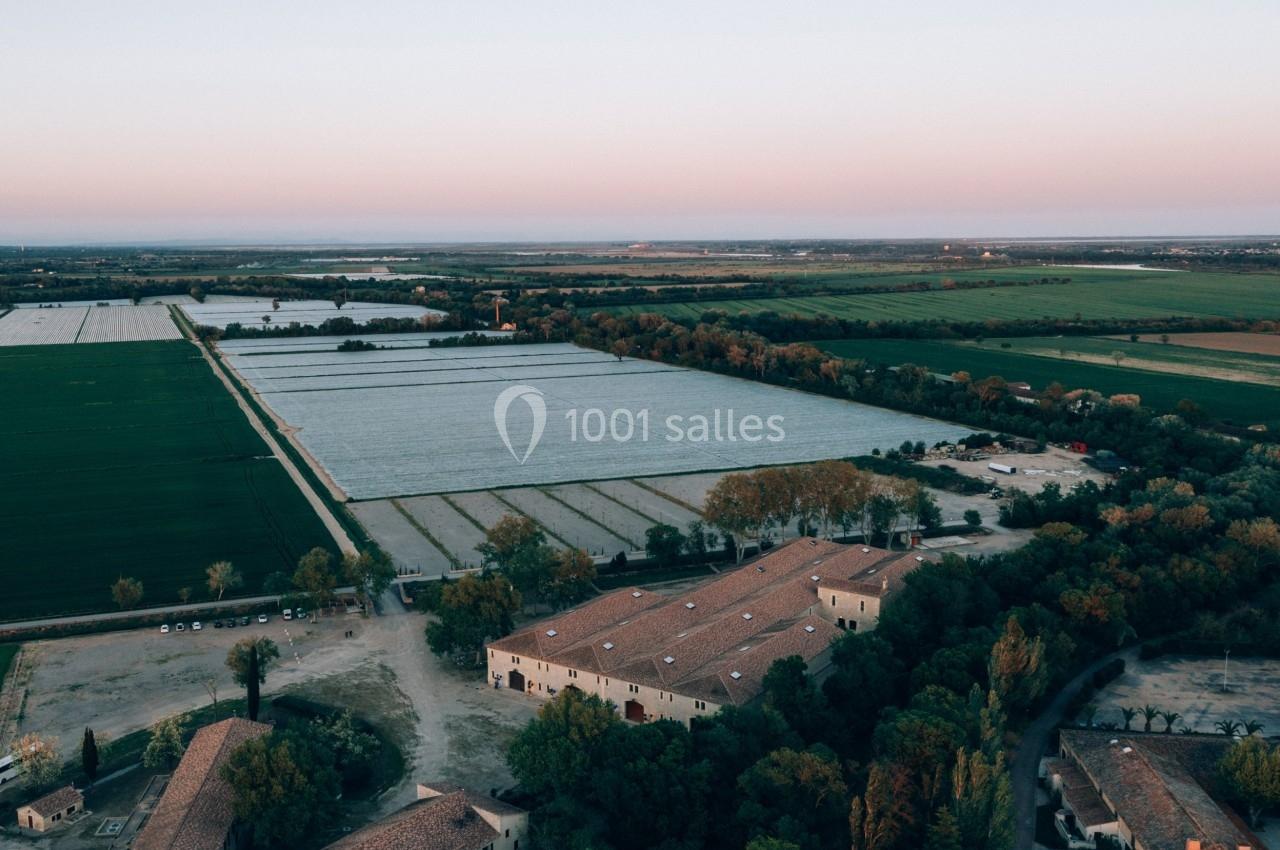 Vue aérienne d'un domaine agricole avec des bâtiments en pierre entourés de champs et d'arbres au coucher du soleil.