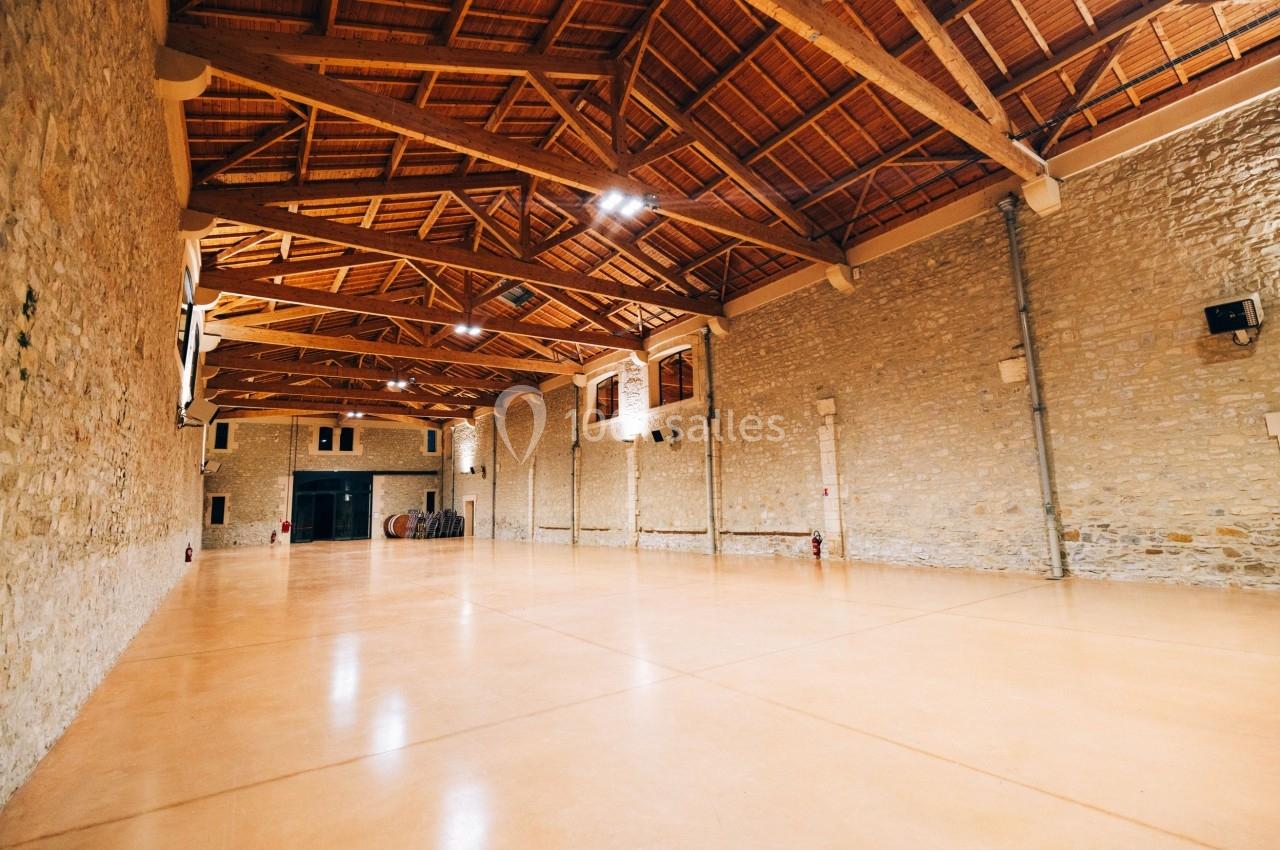 Grande salle avec un sol en béton lisse, murs en pierre et plafond en bois avec poutres apparentes.