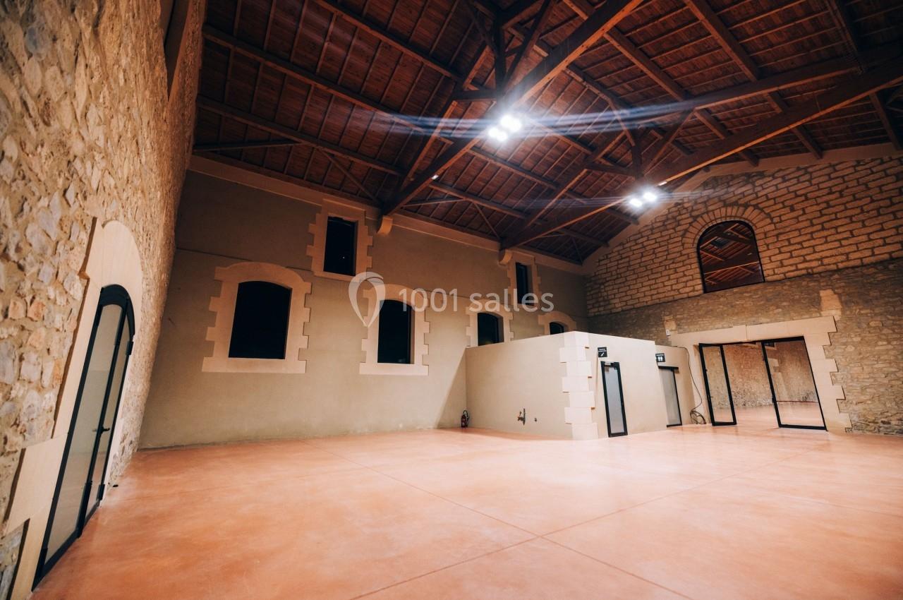 Intérieur d'une grande salle avec murs en pierre, plafond en bois et sol en béton lisse, éclairée par des lumières au…