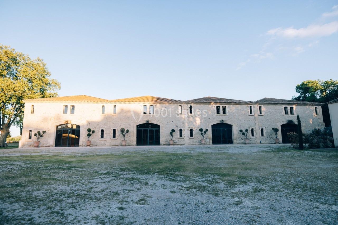 Bâtiment en pierre à deux étages avec grandes portes vitrées, entouré d'arbres et d'une cour dégagée.