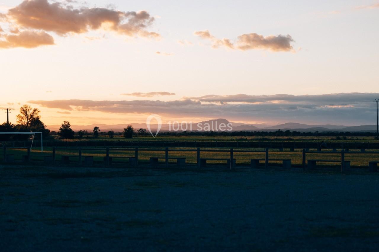 Paysage au coucher du soleil avec des champs, une clôture en bois et des montagnes à l'horizon sous un ciel partiellement…