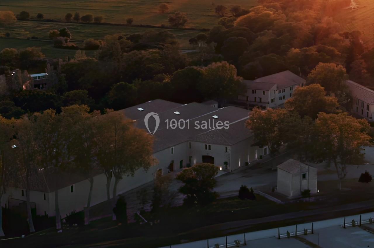 Vue aérienne d'un bâtiment entouré d'arbres au coucher du soleil, avec des champs en arrière-plan.