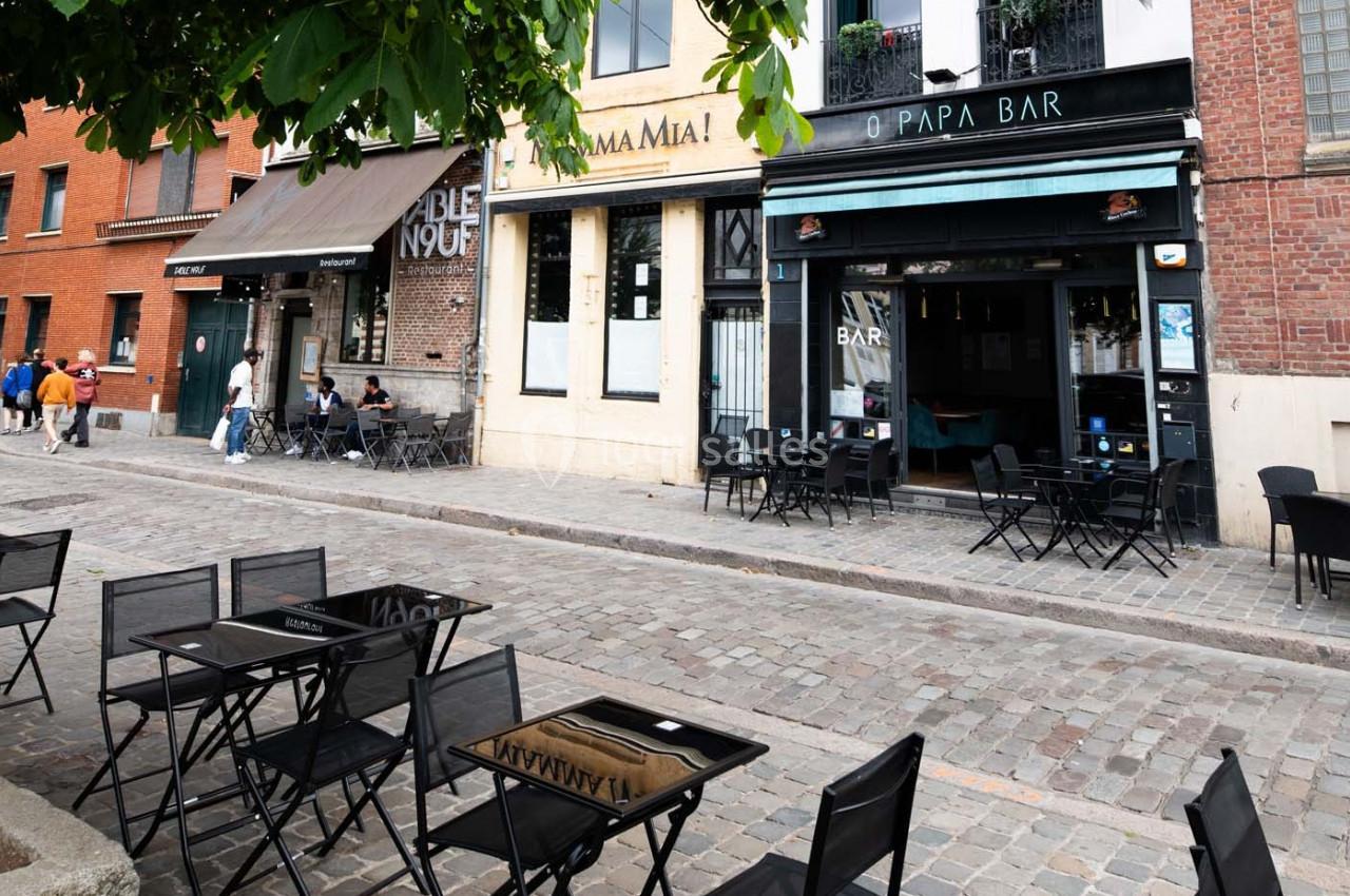 Terrasse vide de cafés et restaurants sur une rue pavée bordée de bâtiments en briques et en pierre.