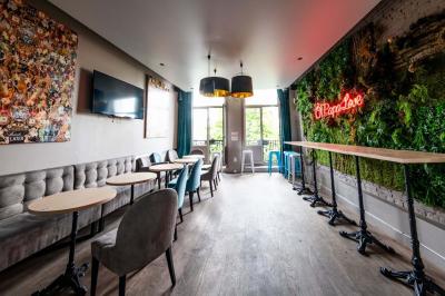 Terrasse vide avec tables et chaises noires sur une rue pavée, devant des façades de cafés et restaurants.