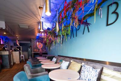 Terrasse vide avec tables et chaises noires sur une rue pavée, devant des façades de cafés et restaurants.