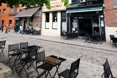 Terrasse vide avec tables et chaises noires sur une rue pavée, devant des façades de cafés et restaurants.