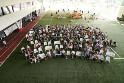 Table ronde en bois entourée de chaises à motifs rouges et blancs, située dans un jardin avec des plantes et des fleurs.