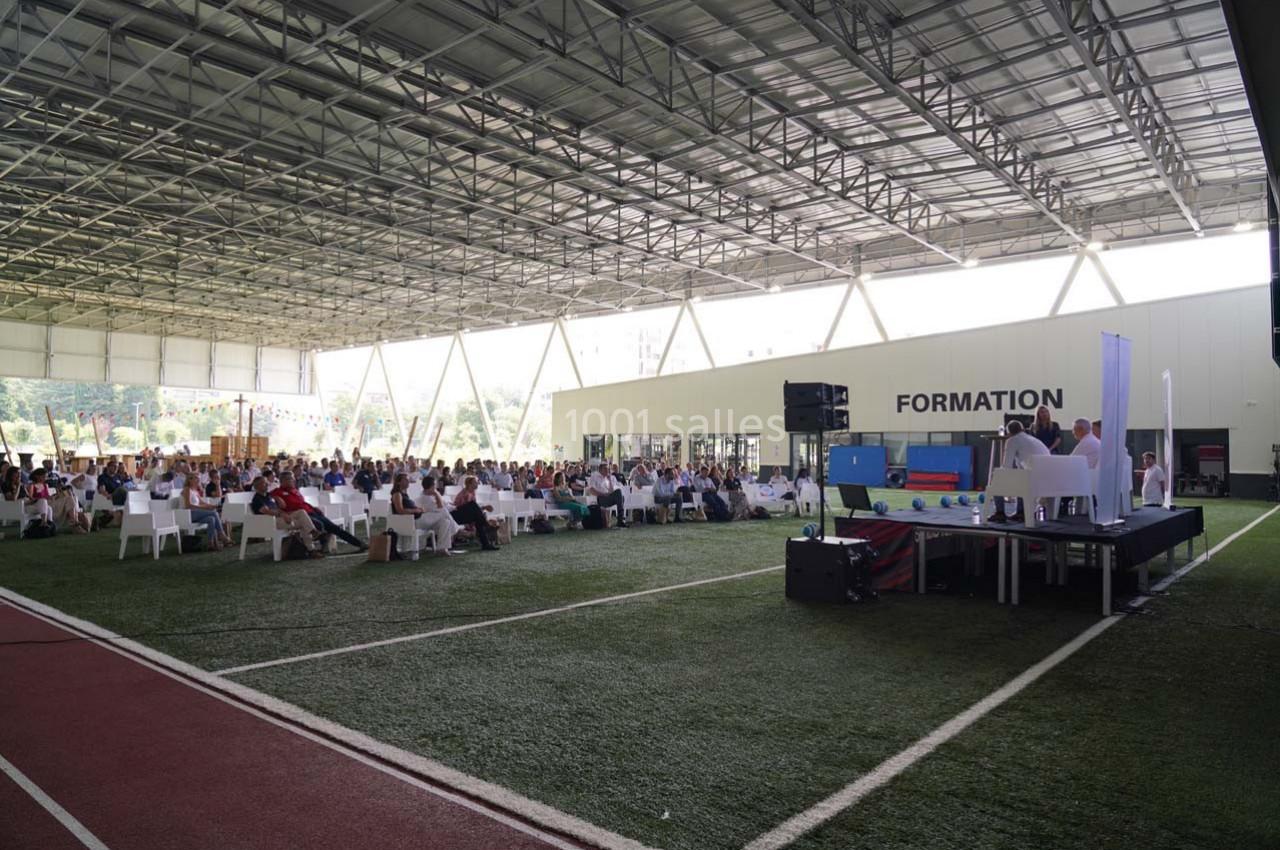 Un groupe de personnes assises sous une structure couverte, assistant à une présentation sur une scène.