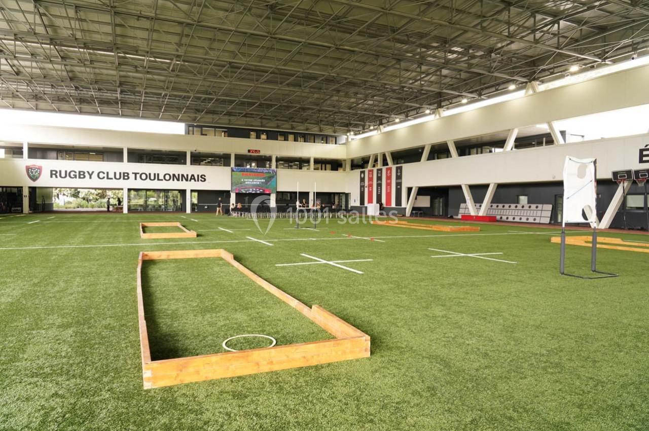Terrain intérieur de rugby avec pelouse synthétique, structures en bois et équipements d'entraînement.