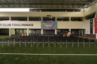 Table ronde en bois entourée de chaises à motifs rouges et blancs, située dans un jardin avec des plantes et des fleurs.
