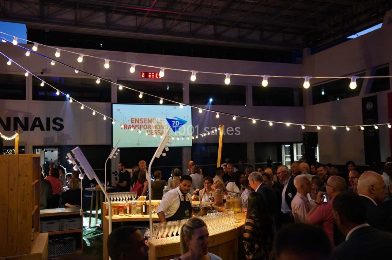 Un groupe de personnes rassemblées dans un espace intérieur éclairé, autour d'un bar en bois, lors d'un événement festif.