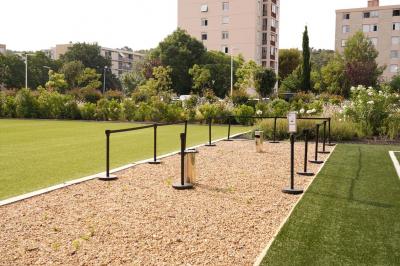 Table ronde en bois entourée de chaises à motifs rouges et blancs, située dans un jardin avec des plantes et des fleurs.