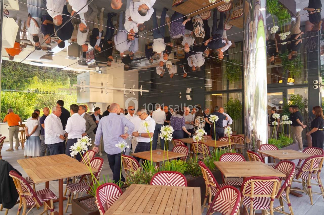 Groupe de personnes échangeant dans un espace extérieur moderne avec tables en bois et plafond réfléchissant.