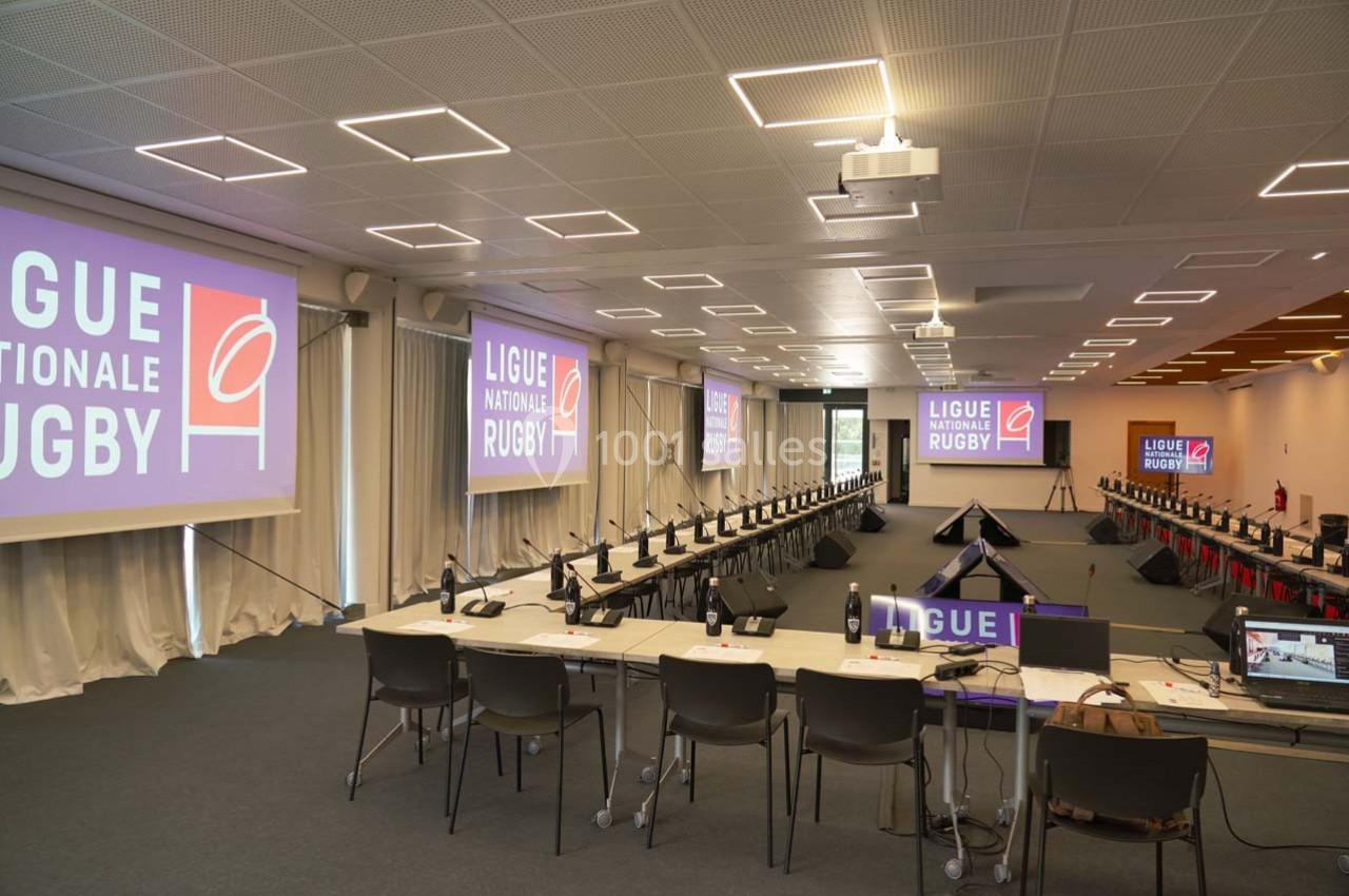 Salle de conférence équipée de tables, chaises, micros et écrans affichant ’Ligue Nationale Rugby’.