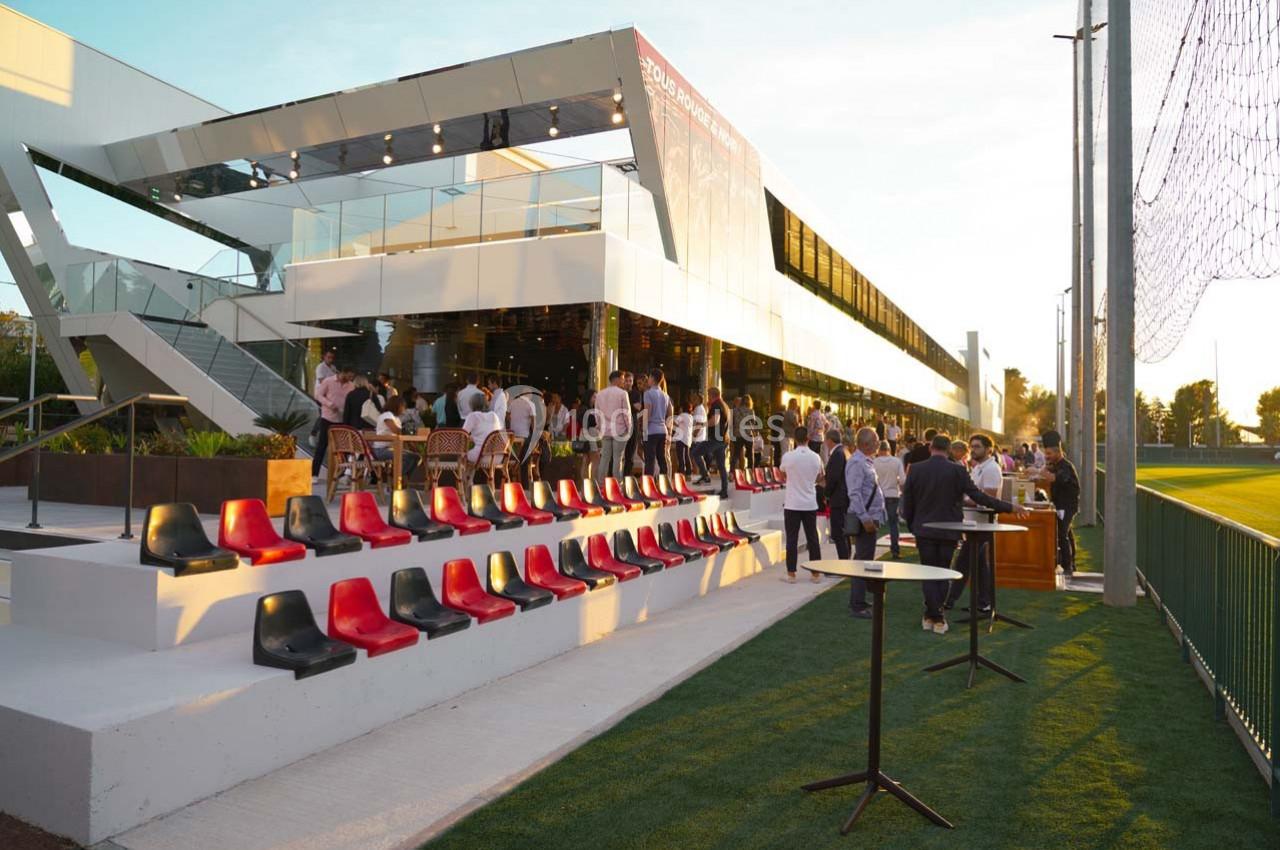 Terrasse moderne avec des sièges colorés, des tables hautes et des personnes rassemblées lors d'un événement en plein air.