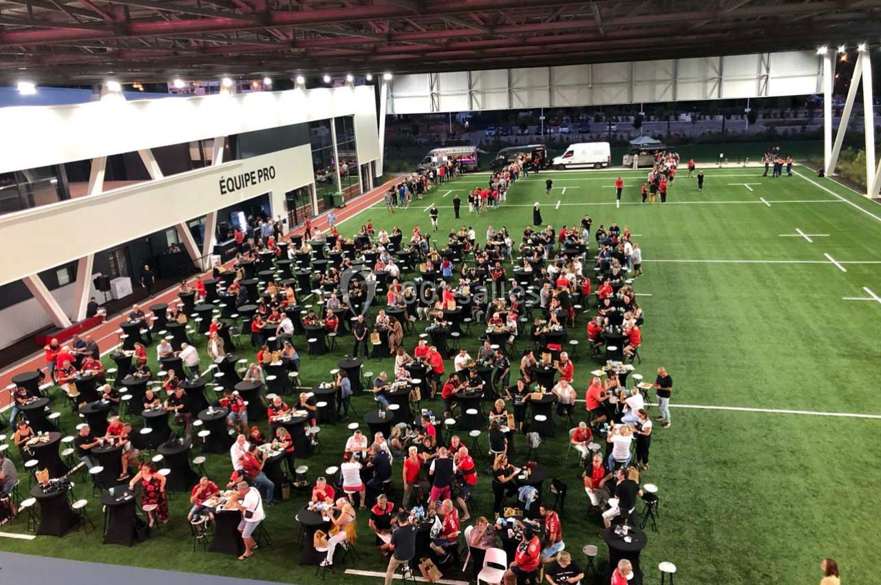 Des personnes assises et debout participent à un événement convivial sur un terrain de sport couvert.