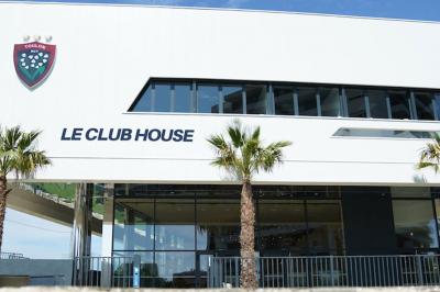 Table ronde en bois entourée de chaises à motifs rouges et blancs, située dans un jardin avec des plantes et des fleurs.