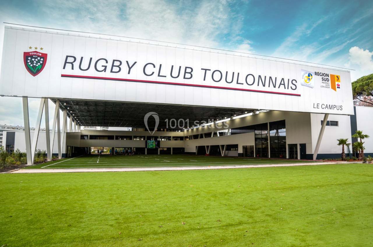 Façade moderne du bâtiment du Rugby Club Toulonnais avec terrain en gazon synthétique au premier plan.