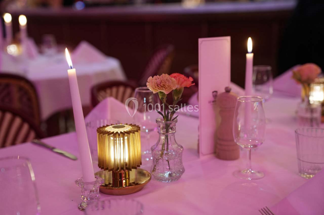Table dressée avec bougies allumées, fleurs dans un vase, verres et accessoires de table dans une ambiance tamisée.