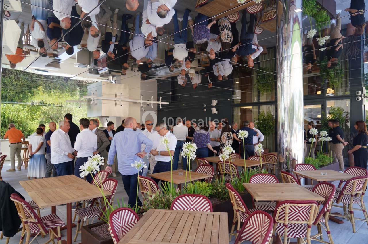 Groupe de personnes discutant dans un espace extérieur moderne avec des tables en bois et un plafond réfléchissant.