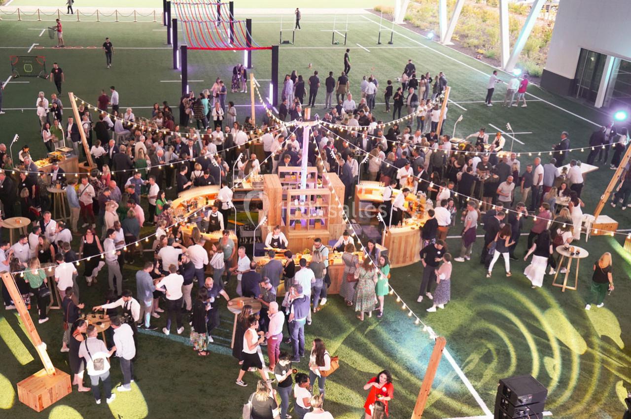 Vue aérienne d'un événement en plein air avec des stands en bois, des guirlandes lumineuses et une foule rassemblée.