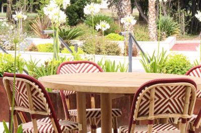 Table ronde en bois entourée de chaises à motifs rouges et blancs, située dans un jardin avec des plantes et des fleurs.