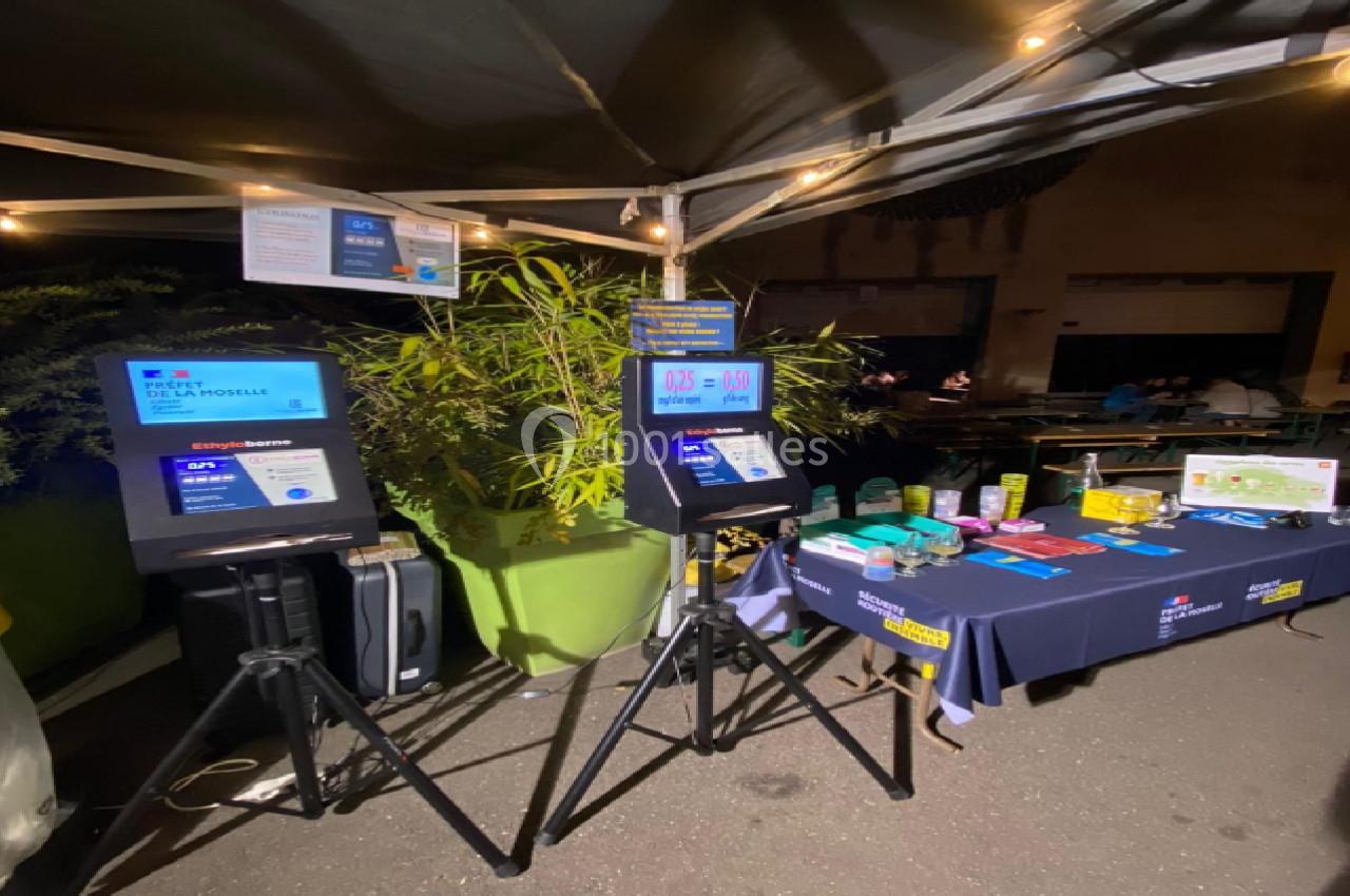 Stand d'information nocturne avec bornes interactives, table d'exposition et éclairage sous une tente.