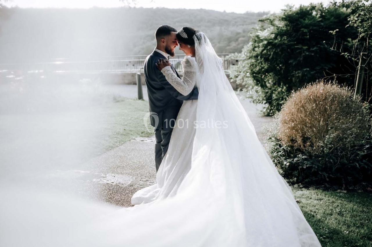 Un couple en tenue de mariage se tient enlacé dans un jardin verdoyant, avec un voile long et fluide.